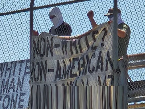 An image of two individuals associated with White Lives Matter Montana demonstrating on an overpass display a sign that reads, “white man zone” and a banner which reads: “Non-white? Non-American.”