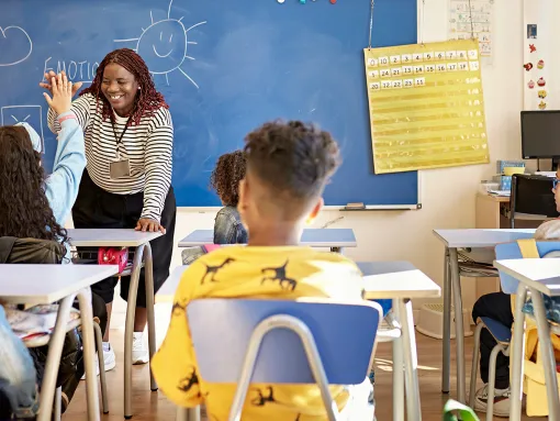 Teacher and Schoolgirl Exchanging High-Five in Classroom