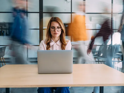 Businesswoman working on laptop in a busy office