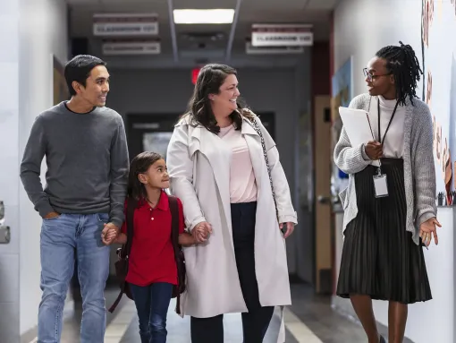 Family walking with their child while talking to teacher in school hallway